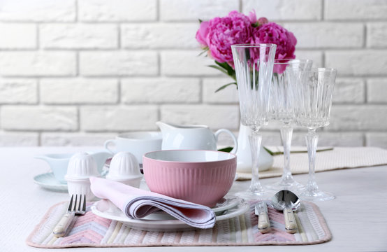 Beautiful table setting with flowers in vase on brick wall background