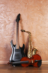 Fototapeta na wymiar Electric guitar, saxophone and violin on brown wall background