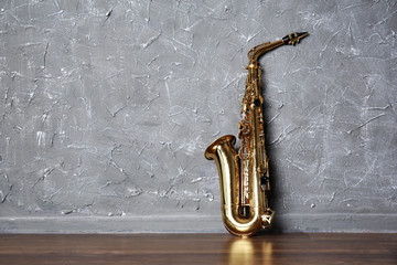 Golden saxophone on gray wall background - obrazy, fototapety, plakaty