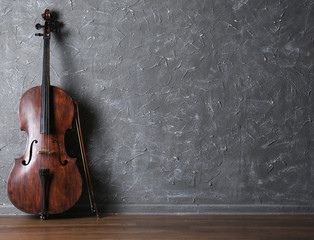Classical cello and bow on gray wall background - obrazy, fototapety, plakaty