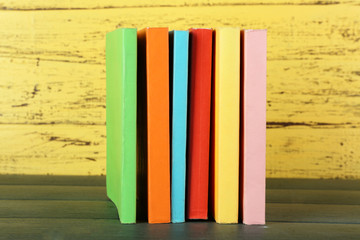 Fototapeta na wymiar Stack of books on wooden table on yellow wooden wall background