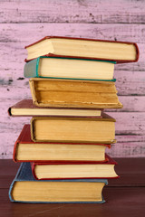 Stack of books on wooden table on pink wooden wall background