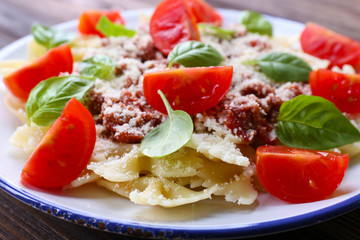 Pasta bolognese with cherry tomatoes in white plate on wooden table, closeup