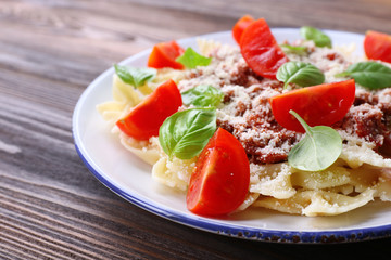 Pasta bolognese with cherry tomatoes in white plate on wooden table, closeup