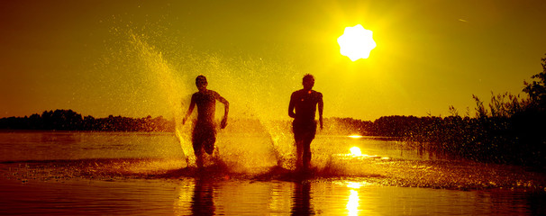 Glückliche junge Menschen laufen und springen am See beim Sonnenuntergang