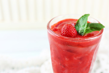 Strawberry dessert with ice in glass, on wooden table, on light background