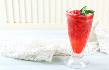 Strawberry dessert with ice in glass, on wooden table, on light background