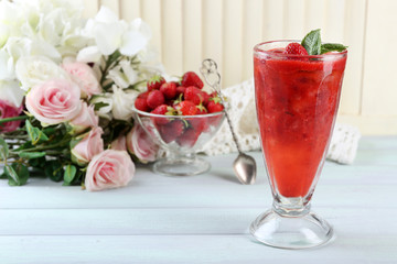 Strawberry dessert with ice in glass, on wooden table, on light background
