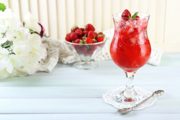 Strawberry dessert with ice in glass, on wooden table, on light background