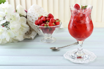 Strawberry dessert with ice in glass, on wooden table, on light background
