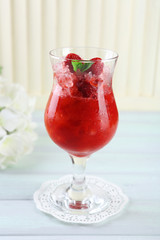 Strawberry dessert with ice in glass, on wooden table, on light background