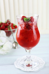 Strawberry dessert with ice in glass, on wooden table, on light background