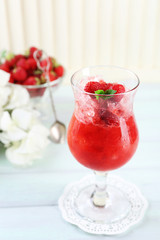 Strawberry dessert with ice in glass, on wooden table, on light background