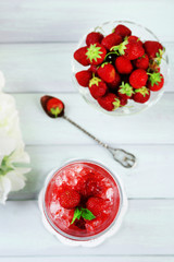 Strawberry dessert with ice in glass, on wooden table, on light background
