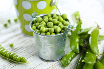 Fresh green peas in metal buckets on white wooden table, closeup