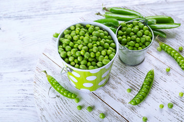 Fresh green peas in metal buckets on white wooden table, closeup