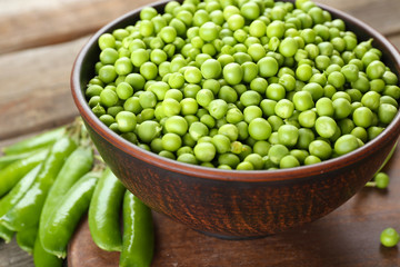 Fresh green peas in clay bowl on wooden cutting board, closeup