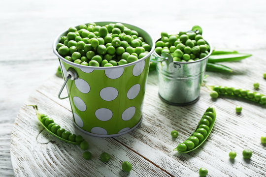 Fresh green peas in metal buckets on white wooden table, closeup