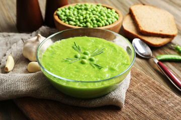 Green pea soup in glass bowl on wooden cutting board with sackcloth, closeup