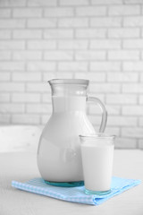 Pitcher and glass of milk on wooden table, on bricks wall background