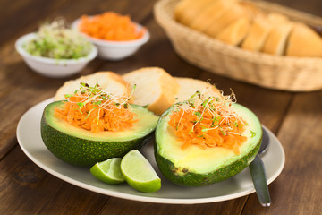 Avocado halves filled with grated carrot and sprinkled with alfalfa sprouts served on plate with lime wedges and baguette slices (Selective Focus, Focus on the front of the grated carrot)