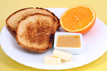 served european breakfast: toasts with butter, orange and orange jam on yellow background
