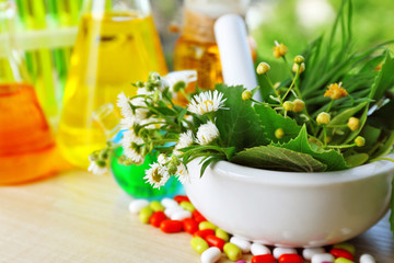 Herbs in mortar, test tubes and pills,  on table background