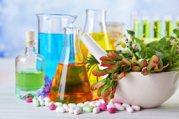 Herbs in mortar, test tubes and pills,  on table, on light background