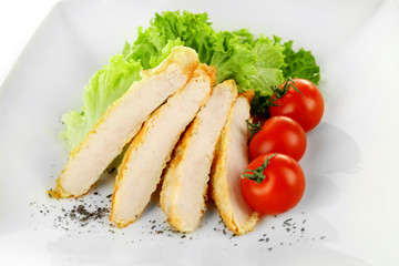 Slices of chicken fillet with cherry tomato and lettuce on plate close up