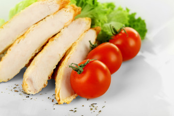 Slices of chicken fillet with cherry tomato and lettuce on plate close up