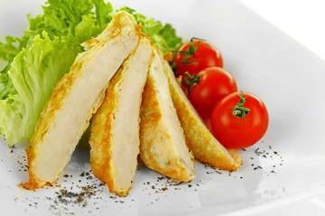 Slices of chicken fillet with cherry tomato and lettuce on plate close up