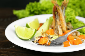 Fried small fish with carrot and greens on table close up