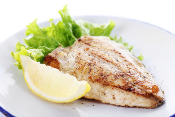 Dish of fish fillet with lettuce and lemon on plate close up