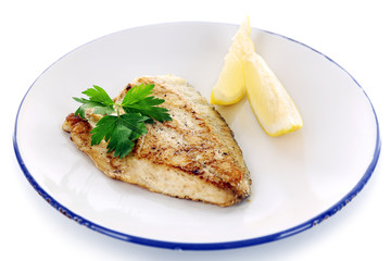Dish of fish fillet with greens and lemon on plate isolated on white