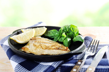 Dish of fish fillet with basil and lemon on bright background