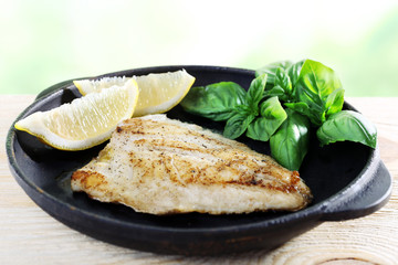 Dish of fish fillet with basil and lemon on bright background