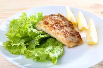 Dish of fish fillet with lettuce and lemon on table close up