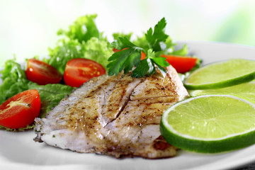 Dish of fish fillet with salad and lime on bright background