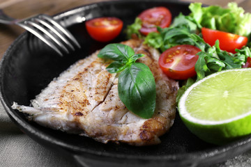 Dish of fish fillet with salad and lime on dripping pan close up