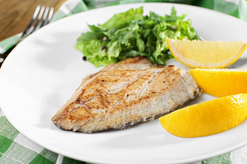 Dish of fish fillet with greens and lemon on plate close up