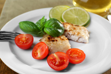 Dish of fish fillet with basil and tomato on plate close up