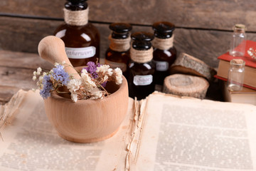 Old book with dry flowers in mortar and bottles on table close up