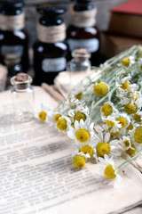 Old book with dry flowers and bottles on table close up