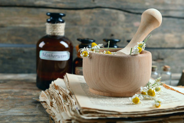 Old book with dry flowers in mortar and bottles on table close up