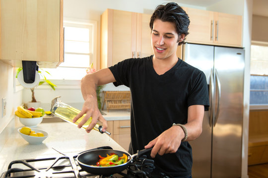 Single young adult male handsome chef alone at home puts olive vegetable oil in frying pan