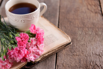 Old book with beautiful flowers and cup of tea on wooden table close up