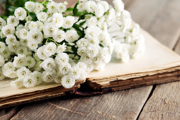 Old book with beautiful flowers on wooden table close up