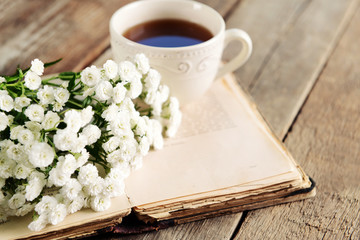Old book with beautiful flowers and cup of tea on wooden table close up
