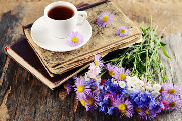 Old books with beautiful flowers and cup of tea on wooden table close up