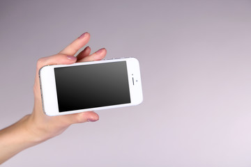 Female hand holding mobile smart phone on gray background